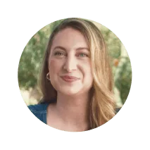 Smiling woman with long blonde hair wearing a denim top, shown in a circular coral frame with a blurred outdoor background. Represents warmth, encouragement, and Noom’s supportive health and wellness community.