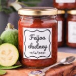 Feijoa chutney 18 Close up jar of homemade feijoa chutney on a board, with vintage spoon and fresh feijoas, stacked jars of chutney in the background.