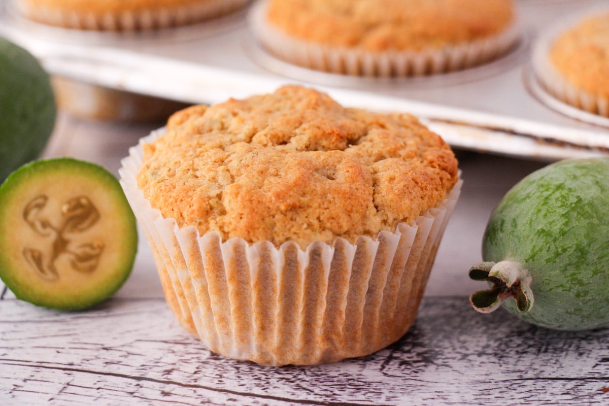 Feijoa muffins with fresh feijoas and feijoa leaves, with extra muffins in muffins tins in the background.