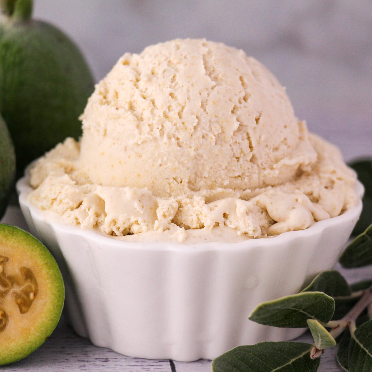 Scoop of feijoa ice cream with fresh feijoa, vintage spoon and sprig of feijoa leaves.