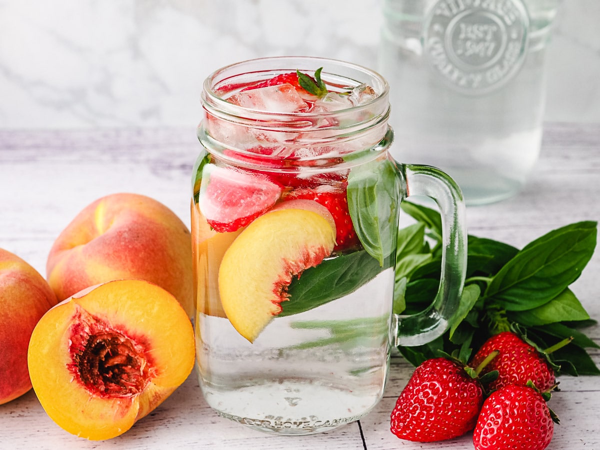 Peach infused water with strawberry and basil with fresh ingredients on the side.