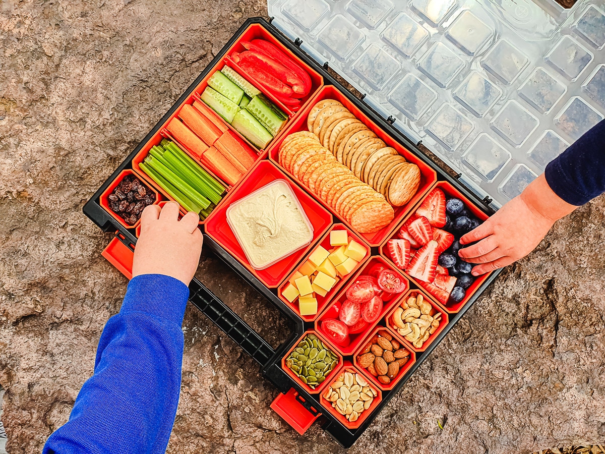 Charcuterie board with kids hands reaching in to take something.