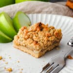 Close up piece of apple slice on a plate with a fork and fresh apple on the side.