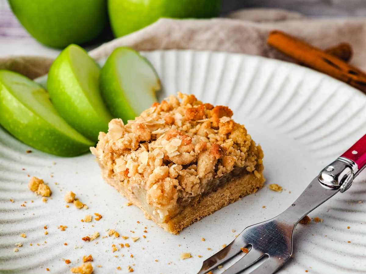 Piece of apple slice on a plate with a fork and fresh apple on the side.