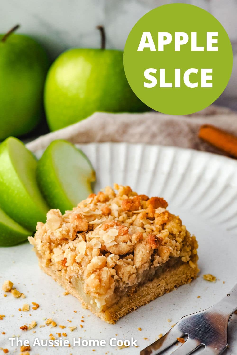 Piece of apple slice on a plate with a fork and fresh apple on the side and fresh apples in the background.